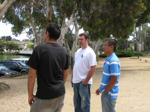 2003 Ford Taurus - Three men are standing in a park near a body of water, with trees overhead.