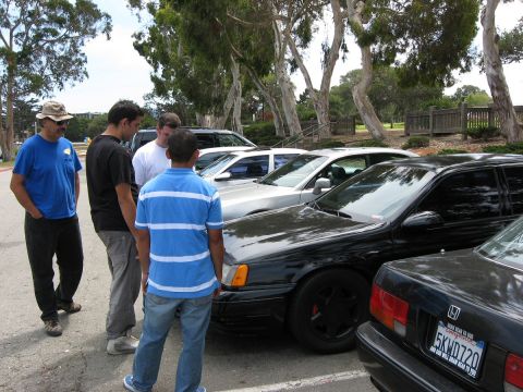 2003 Ford Taurus - Several men stand around a collection of cars parked outdoors on a sunny day.