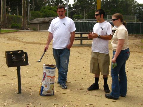 2003 Ford Taurus - Three people are gathered around a park grill and a bag of charcoal, preparing for a barbecue.