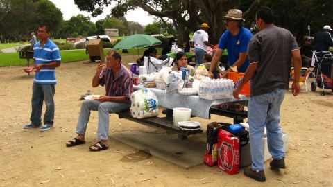 2003 Ford Taurus - People gather around a picnic table loaded with food, paper towels, bottled water and cases of Coca-Cola and A&W at an outdoor park cookout…