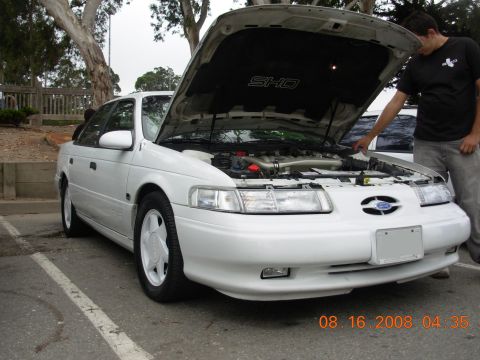 1995 Ford Taurus - A white 1995 Ford Taurus is shown with its hood open, revealing the engine and an SHO emblem on the hood's interior.