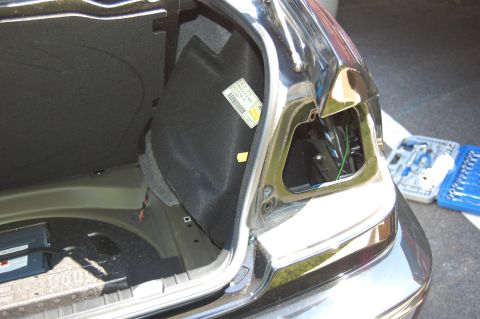 2002 BMW M3 - The rear taillight assembly is removed, revealing the trunk's interior and wiring. Tools are laid out nearby for the repair.