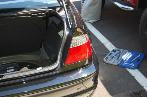 2002 BMW M3 - A set of tools lies on the asphalt next to the open trunk of a car, with a close-up of the taillight visible.