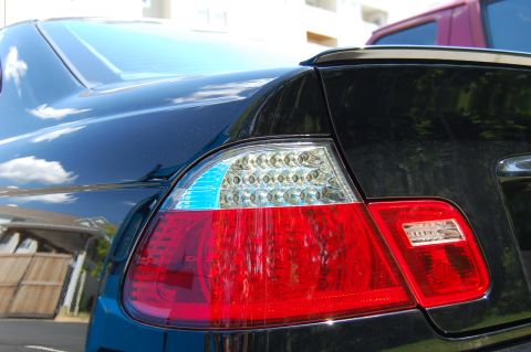 2002 BMW M3 - Rear view of a black car's taillight assembly, showing LED and red brake light components. Another vehicle is visible in the background.