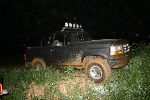1993 Ford Bronco - A black 1992 Ford Bronco is stuck in the mud off-road at night, its tires caked with dirt.