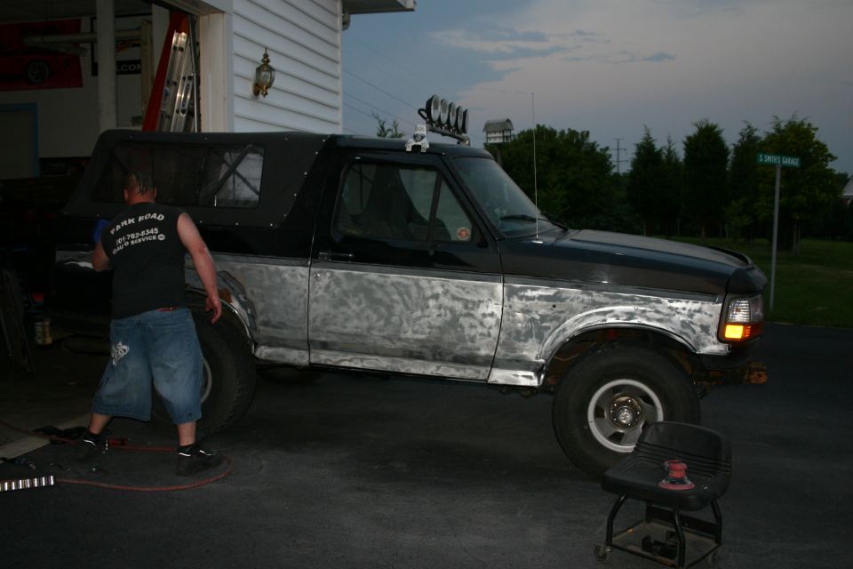 1993 Ford Bronco with primer on the lower body panels, a person is working on it