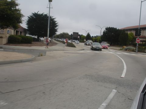 1990 Ford Taurus - Vehicles navigate a street with a pedestrian walkway and surrounding buildings under an overcast sky.