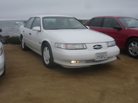 1990 Ford Taurus - A white 1992 Ford Taurus sedan is parked next to a red car with the ocean in the background.