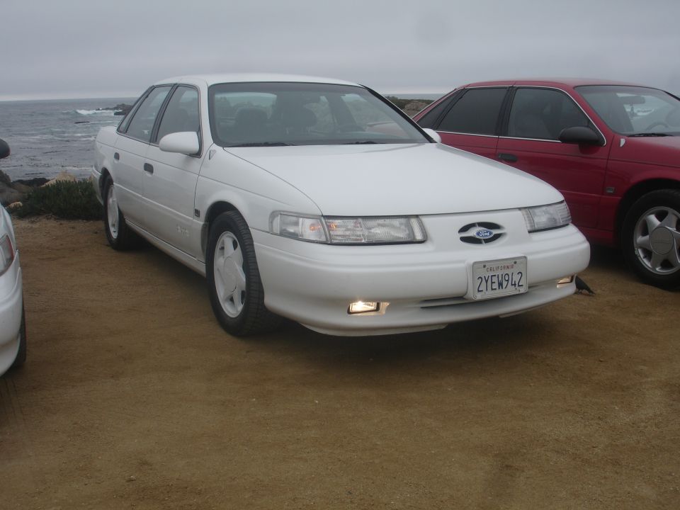 White 1992 Ford Taurus sedan parked on dirt near the ocean, front view