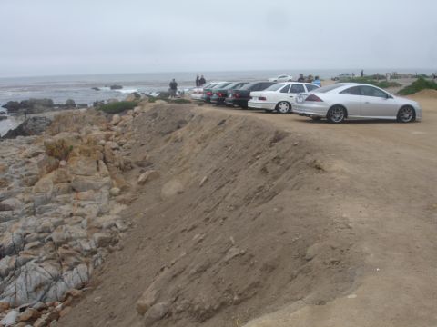 1990 Ford Taurus - Cars are parked along a coastal road with the ocean in the background.