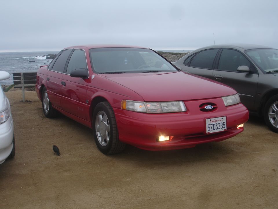 red sedan with California plates parked near the ocean, another car next to it