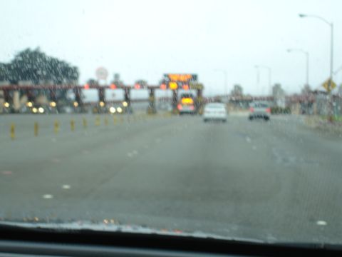 1990 Ford Taurus - Cars approach a toll plaza on a wet day, with traffic lights and signs visible in the distance.