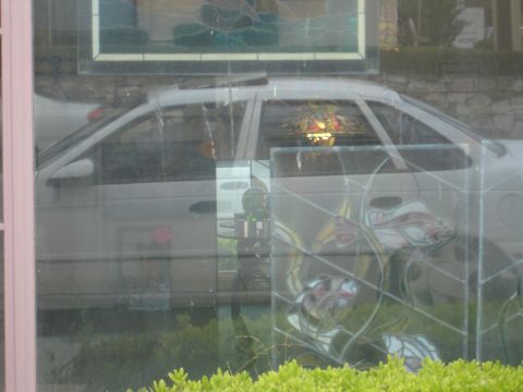 1990 Ford Taurus - A silver sedan is visible through a window, reflecting interior lights and stained glass art.