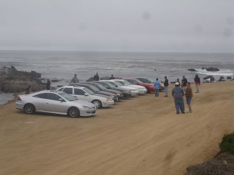 1990 Ford Taurus - A group of cars are gathered on a sandy overlook near the coast on an overcast day.