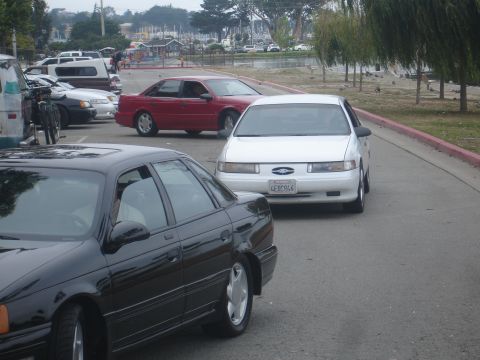 1990 Ford Taurus - A white 1990 Ford Taurus is parked on a street with other vehicles nearby.