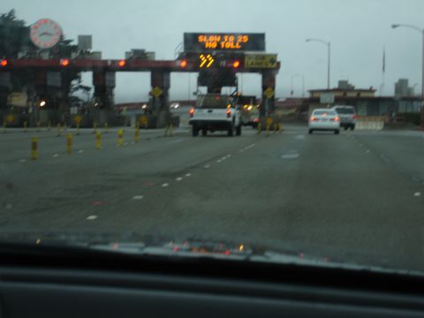 1990 Ford Taurus - Cars approach a toll plaza with electronic signs indicating speed limits and lane information.