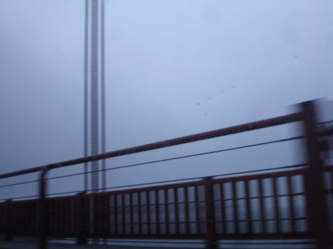 1990 Ford Taurus - A view from a vehicle moving across a bridge shrouded in fog, with a large tower structure visible.