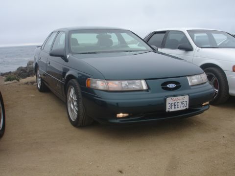 1990 Ford Taurus - A dark green Ford sedan is parked next to a white car with the ocean in the background.