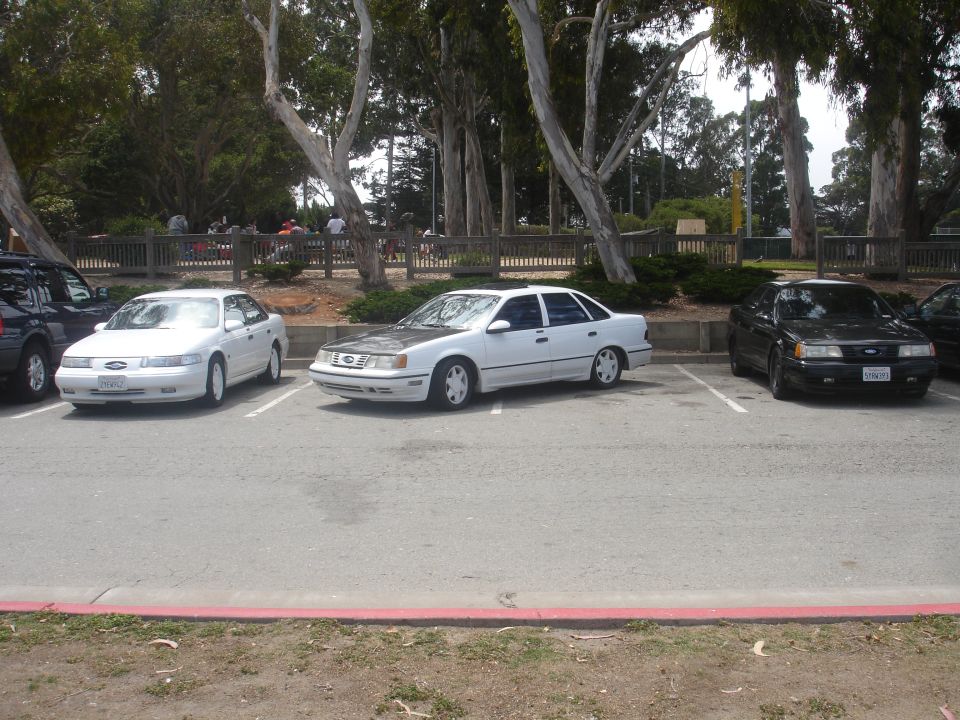 White sedan with a grey hood parked in a lot, front 3/4 view. White wheels, tinted windows