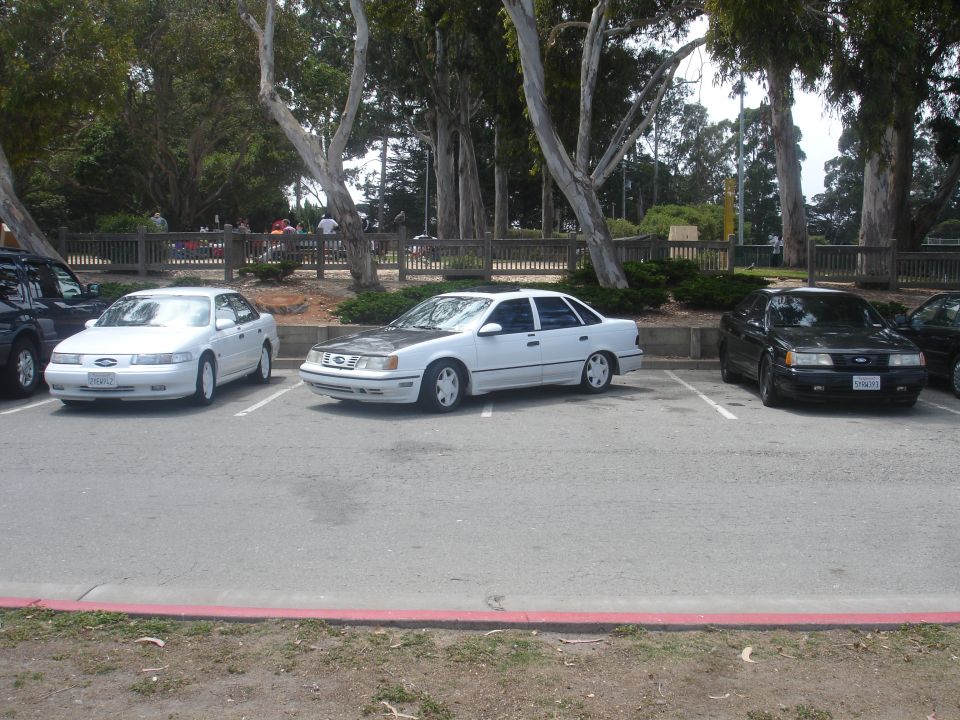 White 1990 Ford Taurus with grey hood parked in a lot