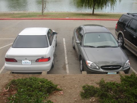 1990 Ford Taurus - Two Ford Taurus sedans and a black SUV are parked in a lot near a body of water.