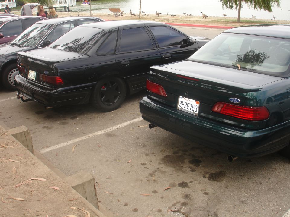 Rear view of a black 1990 Ford Taurus and a dark green 1990 Ford Taurus parked in a lot