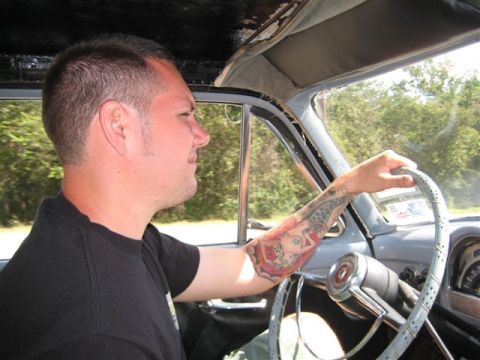 1953 Ford Mainline - A man with tattoos on his arm drives a 1953 Ford Mainline.
