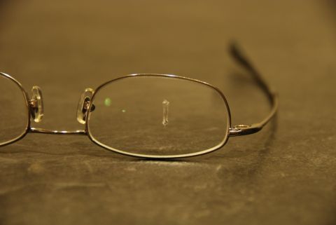 1996 Ford Bronco - Eyeglasses with a small object adhered to the lens, resting on a textured surface.
