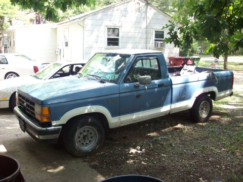 1990 Nissan Sentra - A blue and white Ford Ranger pickup truck is parked in a gravel driveway next to a white car.