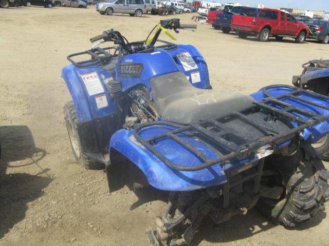 Blue Yamaha Grizzly ATV quad parked in a dusty lot with trucks behind