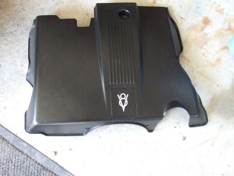 2003 Ford Crown Victoria - A black plastic engine cover with a white V8 emblem is shown laid flat on a concrete surface.