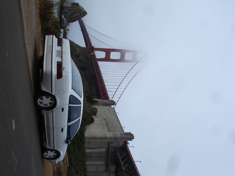 White 1990 Ford Taurus parked near the Golden Gate Bridge on a foggy day.