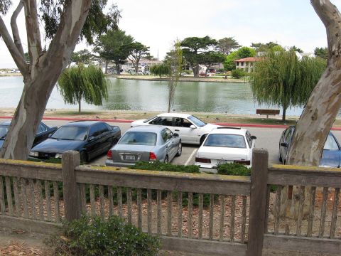 2003 Ford Taurus - Elevated view over a weathered wooden fence of several sedans backed into a lagoon-side parking lot, including a black Ford, a silver sedan…