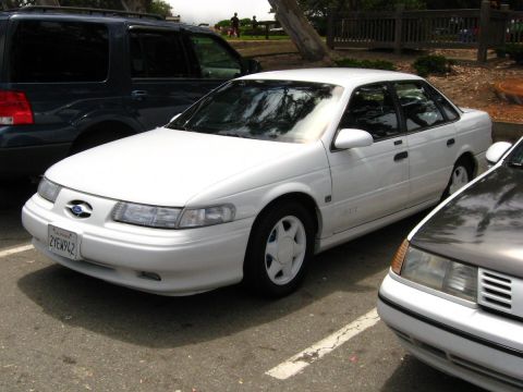 2003 Ford Taurus - Front three-quarter view of a white second-generation Ford Taurus SHO sedan parked in a paved lot, wearing white five-spoke alloy wheels an…
