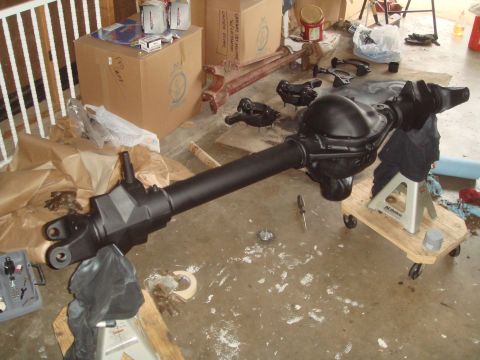 1992 Ford Bronco - A black painted rear axle assembly is supported by a jack stand on a wooden dolly. Various automotive parts and boxes are scattered around…