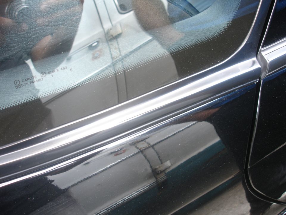 Close-up of black car door trim and windshield with text.