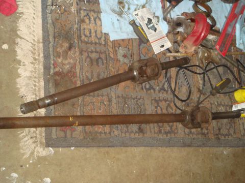 1992 Ford Bronco - Two rusty driveshafts with U-joints are laid out on a patterned rug. Various tools and automotive parts are visible in the background.
