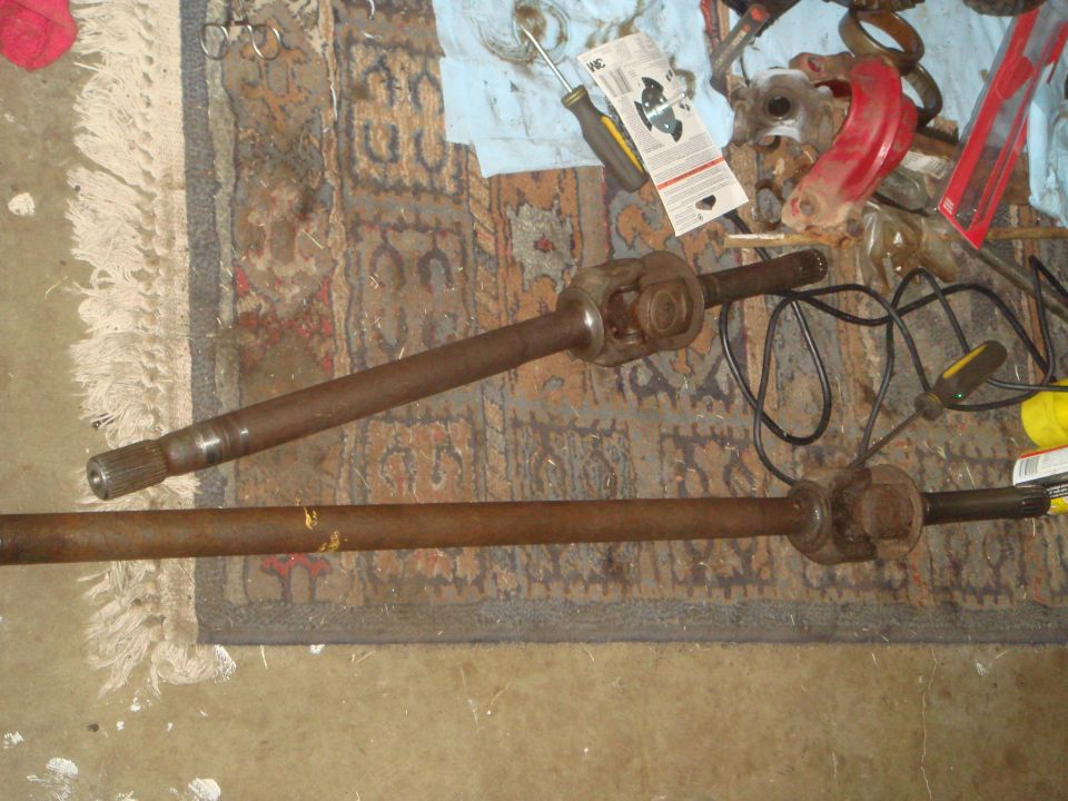 Two rusty driveshafts with U-joints on a rug with tools in the background.