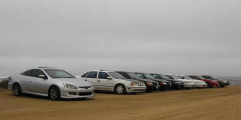 2003 Ford Taurus - Wide shot of a car-meet lineup on a sandy bluff above the ocean: a silver Honda Accord coupe on polished alloy wheels leads a row of white,…