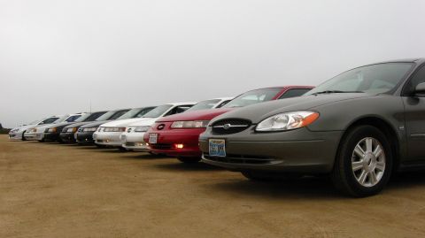 2003 Ford Taurus - Lineup of Ford sedans including gray, red and white cars parked on a dirt lot.