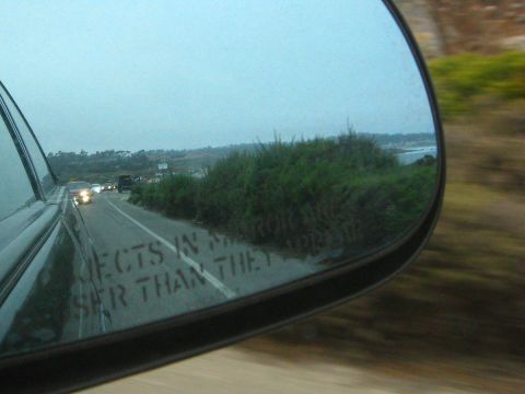 2003 Ford Taurus - Passenger-side mirror shot taken from a moving car, showing the etched "OBJECTS IN MIRROR ARE CLOSER THAN THEY APPEAR" warning and a line o…