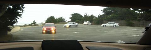 2003 Ford Taurus - View out a car's rear window across an empty coastal parking lot, with a red sedan approaching headlights-on and a white coupe, white SUV a…