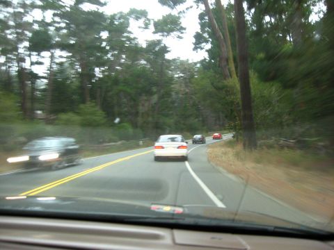2003 Ford Taurus - Windshield view of a white first-generation Ford Taurus sedan leading a cruise on a wooded two-lane road, with a dark car and a red car fur…