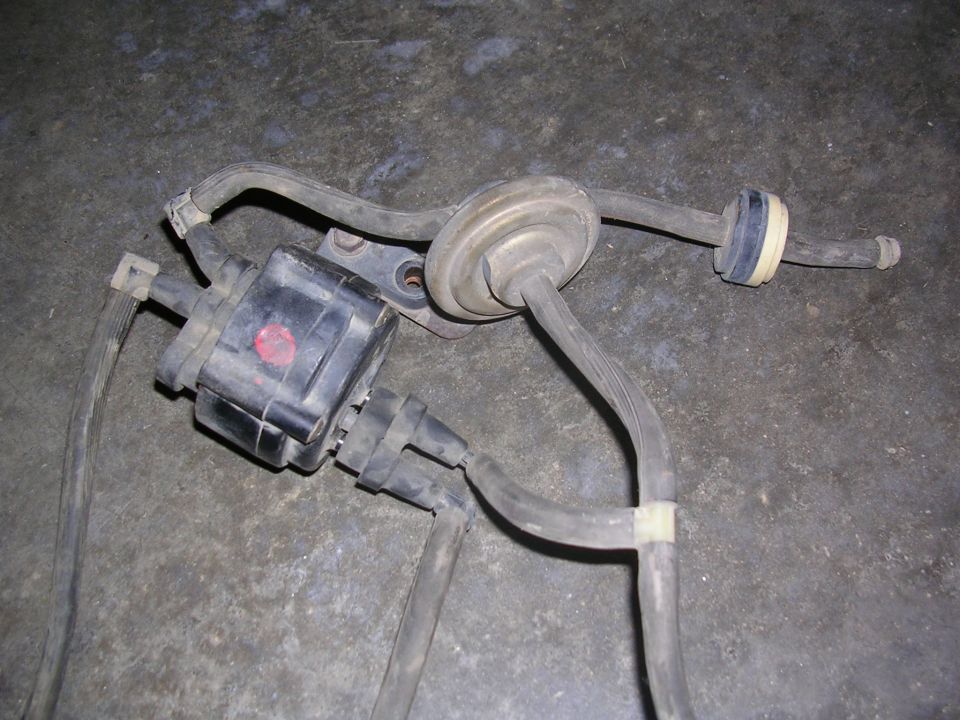 Black ignition coil with vacuum lines and a diaphragm actuator on a concrete surface.
