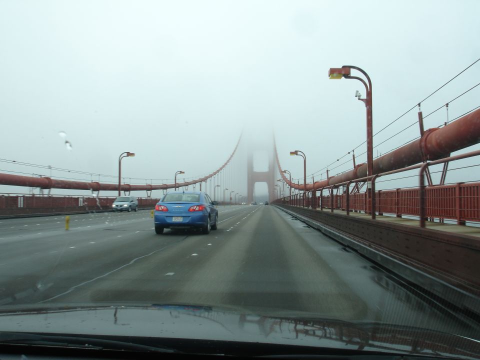 Blue sedan driving on the Golden Gate Bridge in fog.