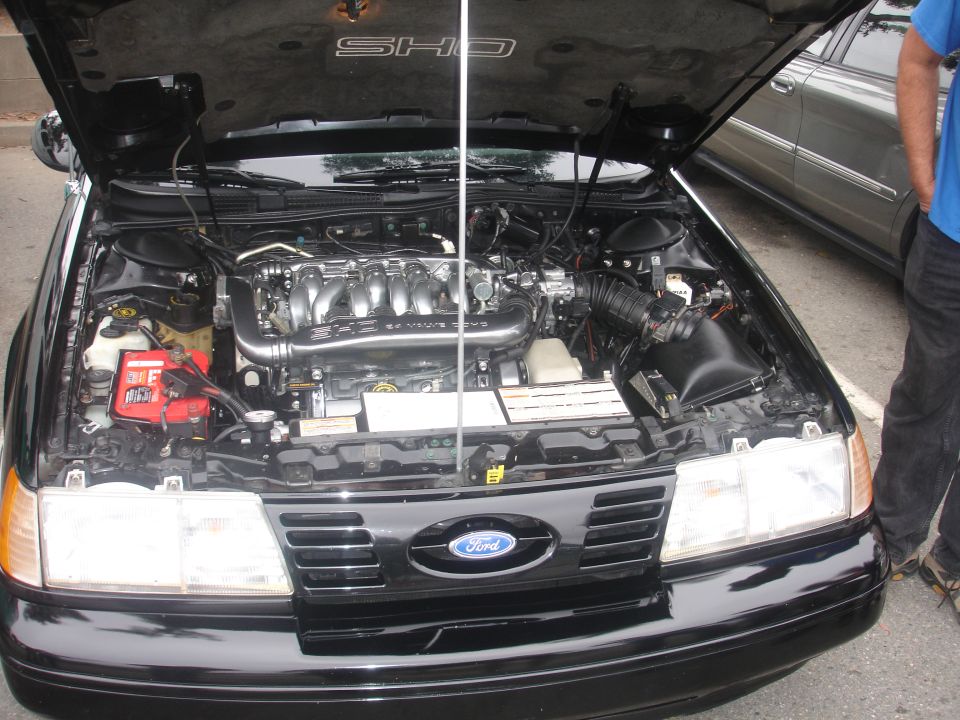 1990 Ford Taurus SHO engine bay with hood open, showing V6 engine, battery, and front grille.