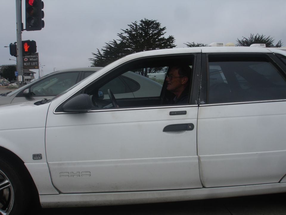 White sedan, side view, driver visible through window, overcast sky
