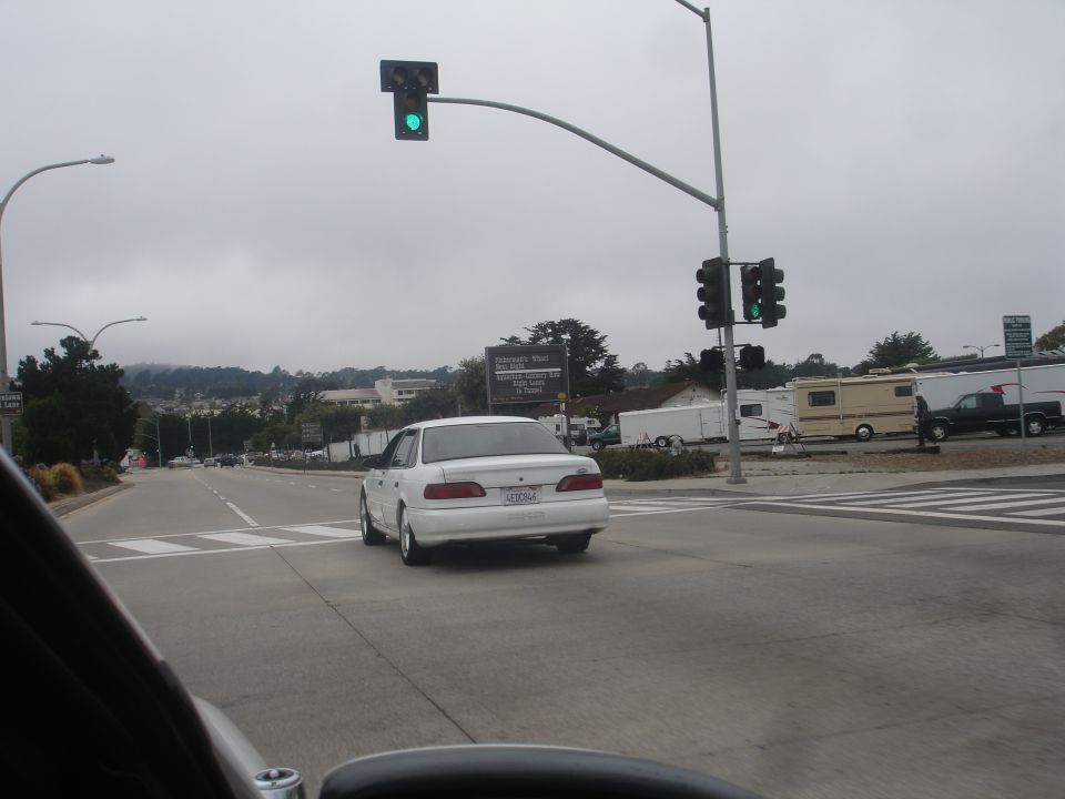 White sedan from rear, driving on a cloudy day