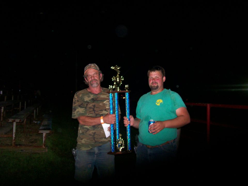 Two men holding a blue-columned trophy outdoors at night
