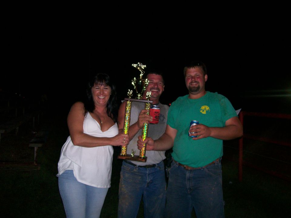 Three people at night holding a tall gold 2008 trophy with a truck topper
